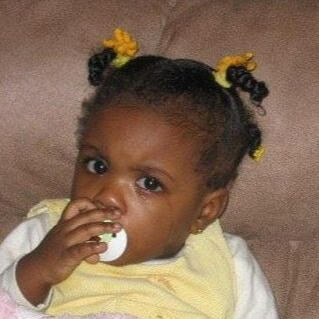 pissed off baby me me (bryce), a couple months old. i have a pacifier in my mouth, pigtail twists with little yellow barettes, and a cream + yellow shirt on. i look very peeved and have, visibly, just finished crying.